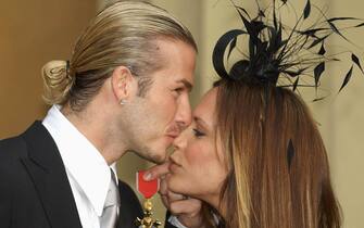 England football captain David Beckham kisses his wife, Victoria, as he holds the OBE (Officer of the Order of the British Empire) he received Thursday November 27, 2003, from Britain's Queen Elizabeth II at London's Buckingham Palace. The former Manchester United star, who now plays for Real Madrid, said recently: 'I am honoured and privileged to receive this recognition. It's not just for me but for Manchester United, England, all of my team mates and my family'. See PA story ROYAL Beckham. PA photo: Fiona Hanson / WPA Rota. 