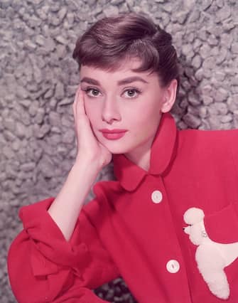 circa 1955:  Headshot portrait of Belgian-born actor Audrey Hepburn (1929 - 1993) leaning on her hand in a red jacket with a poodle applique.  (Photo by Hulton Archive/Getty Images)