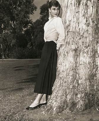 Belgian-born actress, Audrey Hepburn (1929-1993) standing against a tree in a publicity photograph circa 1950s.