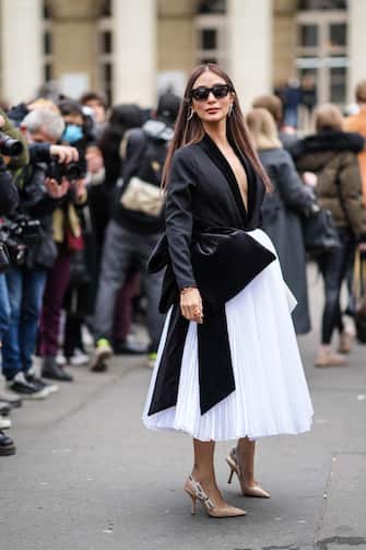 PARIS, FRANCE - JANUARY 27: Heart Evangelista wears black sunglasses, silver pendant earrings, a black V-neck body jacket, a white high waist pleated / accordion oversized midi skirt, a black oversized knot belt, gold rings, beige shiny leather pointed J 'adior slingback pumps heels shoes, outside Fendi, during Paris Fashion Week - Haute Couture Spring / Summer 2022, on January 27, 2022 in Paris, France.  (Photo by Edward Berthelot / Getty Images)