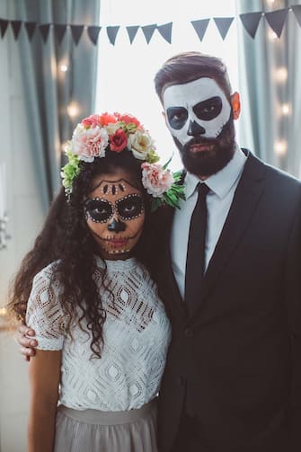 Portrait of young woman with Sugar skull creative make-up and man with make-up costume of skeleton in suit, ready for Halloween party