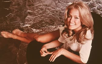 Portrait of American actress Farrah Fawcett dressed in a shirt as she sits and stretched her bare legs, early 1970s. (Photo by Fotos International/Getty Images)