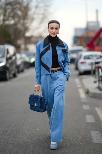 MILAN, ITALY - FEBRUARY 24: Mary Leest wears gold earrings, a black turtleneck pullover, a blue denim with embroidered black fringed pattern jacket, matching blue denim large pants, a black shiny leather belt, a blue denim jeans checkered print pattern Chanel 19 handbag from Chanel, pale blue shiny vanished leather platform high heels pumps heels shoes, outside the MM6 fashion show, during the Milan Fashion Week Fall/Winter 2022/2023 on February 24, 2022 in Milan, Italy. (Photo by Edward Berthelot/Getty Images)