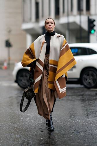 LONDON, ENGLAND - FEBRUARY 16: Camila Carril wears a black turtleneck pullover, a brown skirt, a white brown and orange poncho plaid / cape, a Fendi monogram bag, during London Fashion Week Fall Winter 2020 on February 16, 2020 in London, England .  (Photo by Edward Berthelot / Getty Images)