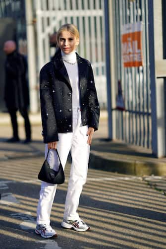 LONDON, ENGLAND - FEBRUARY 17: Caroline Daur wears a white turtleneck pullover, a chain necklace, a black oversized blazer jacket with flared sleeves and printed stars/dots, white pants, sneakers from Asics, during London Fashion Week February 2020 on February 17, 2020 in London, England. (Photo by Edward Berthelot/Getty Images)