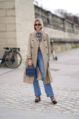 PARIS, FRANCE - FEBRUARY 25: Camille Charriere wears sunglasses, a trench coat, blue denim jeans pants, a Dior blue mini shopping bag, black shoes, a scarf, outside Dior, during Paris Fashion Week - Womenswear Fall/Winter 2020/2021, on February 25, 2020 in Paris, France. (Photo by Edward Berthelot/Getty Images)