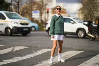 1210430994 PARIS, FRANCE - MARCH 03: Sophia Roe wears sunglasses, a white polo shirt, a green pullover from Lacoste, a white pleated mini skirt, white socks, sneakers, outside Lacoste, during Paris Fashion Week - Womenswear Fall/Winter 2020/2021 on March 03, 2020 in Paris, France. (Photo by Edward Berthelot/Getty Images)