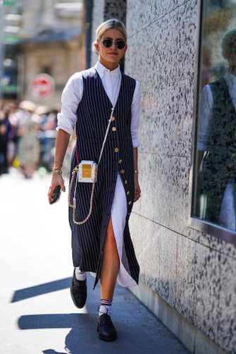 1157729901 PARIS, FRANCE - JUNE 22: Caroline Daur wears sunglasses, a white long shirt dress, a sleeveless striped long jacket, a mini bag with golden inserts, striped socks, black shoes, outside Thom Browne, during Paris Fashion Week - Menswear Spring/Summer 2020, on June 22, 2019 in Paris, France. (Photo by Edward Berthelot/Getty Images)