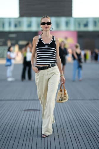 COPENHAGEN, DENMARK - AUGUST 11: Pernille Teisbaek wears black sunglasses, black and white large Coco earrings from Chanel, a black and white striped print pattern tank-top from Chanel, a black shiny leather belt, beige denim wide legs pants, a beige wicker with a camel leather handle handbag, silver and gold large chain bracelet, a gold ring, black shiny varnished leather / open toe-cap / pointed pumps heels shoes , outside Ganni, during Copenhagen Fashion Week Spring/Summer 2023, on August 11, 2022 in Copenhagen, Denmark. (Photo by Edward Berthelot/Getty Images)