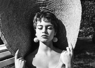 circa 1955:  Headshot of French actor Brigitte Bardot closing her eyes and holding the rim of her straw hat while basking in the sun outdoors. Bardot has brunette hair and wears drop earrings.  (Photo by Express/Express/Getty Images)