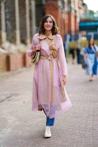 LONDON, ENGLAND - SEPTEMBER 15: Alexa Chung wears a pale pink transparent trench coat with a beige part, a belt, a bag, blue jeans, white sneakers, during London Fashion Week September 2019 on September 15, 2019 in London, England. (Photo by Edward Berthelot/Getty Images)