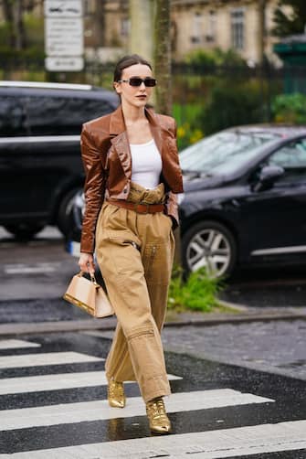 PARIS, FRANCE - MARCH 02: Mary Leest wears sunglasses, a brown shiny jacket, a white t-shirt, a brown leather belt, beige pants with cargo pockets, golden shiny pointy shoes, a triangular shaped bag outside Akris, during Paris Fashion Week - Womenswear Fall/Winter 2020/2021, on March 02, 2020 in Paris, France. (Photo by Edward Berthelot/Getty Images)