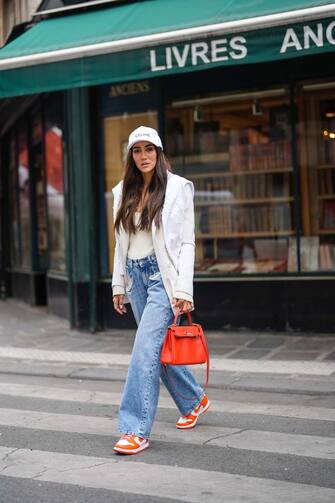 PARIS, FRANCE - APRIL 30: Tamara Kalinic wears a white Celine cap, a gold chain pendant necklace, a white latte ribs tank top, a white long Saint Laurent YSL blazer jacket, a white embroidered Chanel sweater, a red shiny leather Kelly Hermes handbag, blue faded denim boyfriend jeans Margiela pants, red and white shiny leather Nike Air Force 1 sneakers, on April 30, 2021 in Paris, France. (Photo by Edward Berthelot/Getty Images)