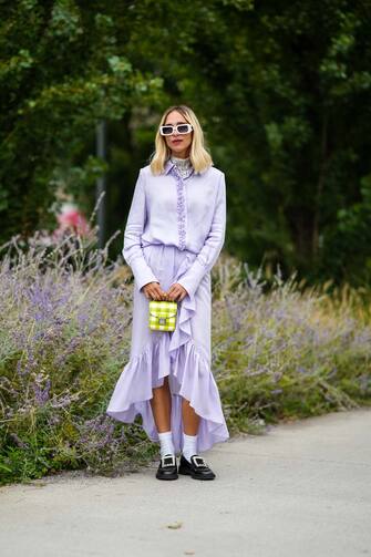 MILAN, ITALY - SEPTEMBER 25: Candela Novembre wears white sunglasses, a silver sequined turtleneck t-shirt, a pale purple buttoned shirt, a pale purple flowing ruffled asymmetric long skirt, a yellow and white checkered print pattern handbag, white socks, black shiny leather loafers with rhinestones buckle, outside the MSGM fashion show during the Milan Fashion Week - Spring / Summer 2022 on September 25, 2021 in Milan, Italy. (Photo by Edward Berthelot/Getty Images)