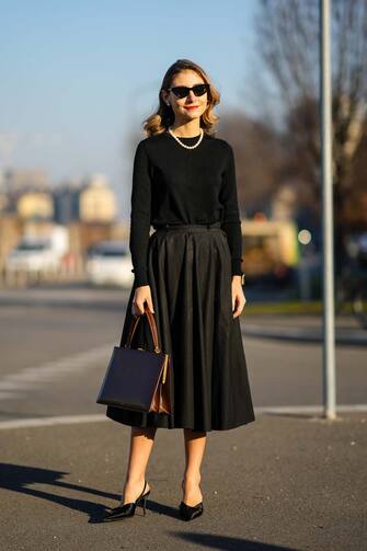 MILAN, ITALY - JANUARY 16: Jenny Walton wears sunglasses, a pearl beaded necklace, a black pullover, a brown rectangular briefcase shaped leather bag from Celine, a black pleated midi skirt, black pointed shoes with high heels, outside the Prada  fashion show during the Milan Men's Fashion Week - Fall/Winter 2022/2023 on January 16, 2022 in Milan, Italy. (Photo by Edward Berthelot/Getty Images)