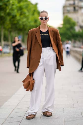 PARIS, FRANCE - JUNE 23: A guest wears white sunglasses, an oversized brown blazer jacket, a black t-shirt, white flare pants, sandals, outside Celine, during Paris Fashion Week - Menswear Spring/Summer 2020, on June 23, 2019 in Paris, France. (Photo by Edward Berthelot/Getty Images)