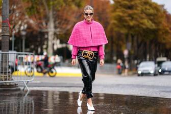 1180684456 PARIS, FRANCE - OCTOBER 01: Sofie Valkiers wears sunglasses, earrings, a pink tweed jacket, a pink short cape, a Chanel belt-bag, shiny black patent leather pants, white pointy heels, outside Chanel, during Paris Fashion Week - Womenswear Spring Summer 2020, on October 01, 2019 in Paris, France. (Photo by Edward Berthelot/Getty Images)
