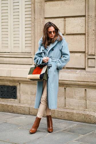 PARIS, FRANCE - NOVEMBER 19: Therese HellstrÃ¶m wears sunglasses, a blue long winter wool trench coat with fluffy faux fur collar, white pants, a fluffy red and green khaki bag, brown leather pointy boots with metallic heels, on November 19, 2020 in Paris, France. (Photo by Edward Berthelot/Getty Images)