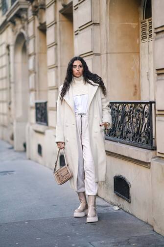 PARIS, FRANCE - DECEMBER 18: Gabriella Berdugo wears a white long coat from Max Mara, a white wool cropped knitted / woven pullover from Max Mara, a white shirt, vintage white jogger sport pants from Camps, a beige pale brown flat leather bag with external pockets from Bottega Veneta, beige silver shiny platform boots from AGL, on December 18, 2020 in Paris, France. (Photo by Edward Berthelot/Getty Images)