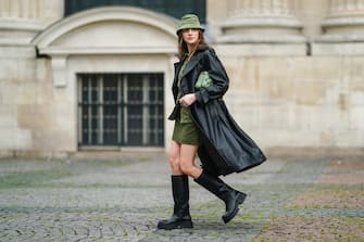 PARIS, FRANCE - FEBRUARY 22: Olesya Senchenko wears a green bob hat from Bagarreuse, a black leather long coat from H&M, a green corduroy jacket from Bagarreuse, a short skirt from Bagarreuse, a green quilted bag from JW Pei, black leather knee high boots from Zara, on February 22, 2021 in Paris, France. (Photo by Edward Berthelot/Getty Images)