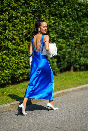 MILAN, ITALY - SEPTEMBER 24: Anna Rosa Vitiello wears beige circle earrings, a royal blue fringed V-backless / asymmetric shoulders long flowing silk dress, white long gloves, white leather with brown tasks handbag, white leather pointed pumps heels shoes from Balenciaga, outside the Sportmax fashion show during the Milan Fashion Week - Spring / Summer 2022 on September 24, 2021 in Milan, Italy.  (Photo by Edward Berthelot / Getty Images)