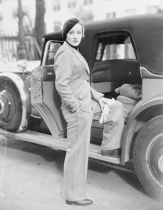 Wearing a beret and carrying gloves, Marlene Dietrich, prominent Paramount screen star, jauntily strolls along Hollywood Street attired in a grey man's suit, with turtle-neck sweater. Stylists declare this mode set by Marlene will sweep the country--which probably means that men will have to find themselves some cute tailored skirts.