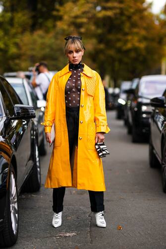 PARIS, FRANCE - SEPTEMBER 28: Sira Pevida wears a headband, a yellow pvc trench coat, a black Fendi logo-embroidered mesh bodysuit, black pants, white shoes, a black and white striped bag, outside Elie Saab, during Paris Fashion Week - Womenswear Spring Summer 2020, on September 28, 2019 in Paris, France. (Photo by Edward Berthelot/Getty Images)