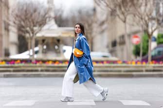 PARIS, FRANCE - MARCH 05: Alexandra Pereira wears a white turtleneck pullover / sweater from Zara, a blue long trench coat from Stand Studio, white flare denim jeans from Zara, an orange half-moon semi-circular bag from Fendi, white sneakers shoes from New Balance, on March 05, 2021 in Paris, France. (Photo by Edward Berthelot/Getty Images)