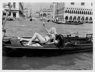 Actress Diana Dors modeling a mink bikini on a gondola, waving to the crowds as she floats along the canal, at the Venice Film Festival, Italy, September 5th 1955. (Photo by Keystone/Hulton Archive/Getty Images)