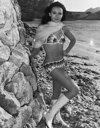 1970:  Full-length portrait of British-born actor and model Lesley-Anne Down posing against sea wall and wearing a bikini, go-go boots, and a scarf during a break in the production of director Vicente Escriva's film, 'Without a Good-bye' ('Sin Un Adios') in which she stars.  At age 15, this is Down's third film.  (Photo by Express/Express/Getty Images)