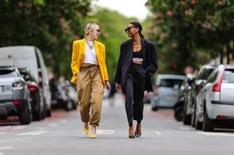 PARIS, FRANCE - MAY 20: Emy Venturini (L) wears black vintage sunglasses, a gold large chain necklace, a white Ipsilonparis t-shirt, a yellow oversized vintage blazer jacket, a gold ring, brown cargo vintage pants, yellow shiny leather pointed pumps heels strappy shoes ; Emilie Joseph (R) wears black sunglasses, a gold ring, a gold large chain necklace, a black Paco Rabanne bra underwear, a long black with white stripes oversized blazer jacket, black with white stripes matching suit pants, black shiny leather pumps / heels shoes, on May 20, 2021 in Paris, France. (Photo by Edward Berthelot/Getty Images)