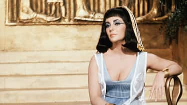 (Original Caption) 1962-Rome, Italy: Elizabeth Taylor as Cleopatra, is shown seated on a chair in front of a stairwell, on the set in Rome where the movie is being shot.
