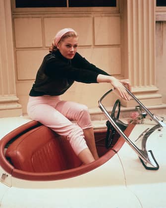 circa 1955:  EXCLUSIVE A portrait of Swedish actor Anita Ekberg sitting on the trunk of a cream convertible with her feet in its red leather interior, Hollywood, California. Ekberg wears cream-colored Capri pants, a black top and a scarf in her hair.  (Photo by Gene Lester/Getty Images)