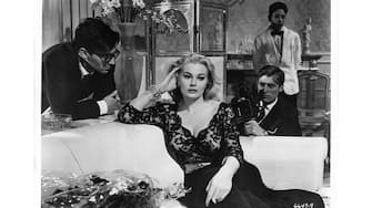 Anita Ekberg on couch brushing back her hair while unidentified men watch in a scene from the film 'La Dolce Vita', 1960. (Photo by American International Pictures/Getty Images)