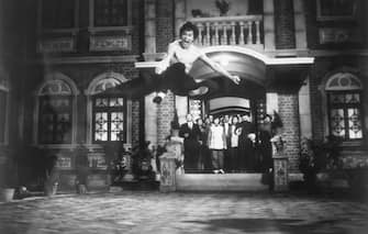 (Original Caption) Bruce Lee demonstrating a Kung-fu kick in the air as people watch on the set of "The Chinese Connection". Undated photo.