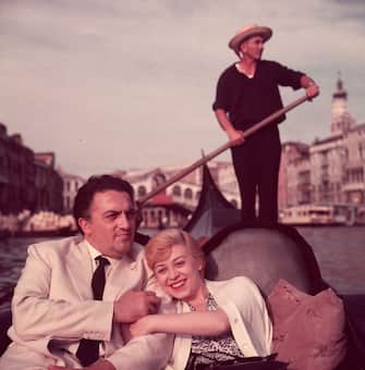 3203012 circa 1955: Italian film director Federico Fellini (1920 - 1993) and his wife, actor Giulietta Masina (1920 - 1994), hold hands and smile while sitting in a gondola with a gondolier rowing in the background, Venice, Italy. (Photo by Hulton Archive/Getty Images)