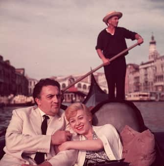 circa 1955:  Italian film director Federico Fellini (1920 - 1993) and his wife, actor Giulietta Masina (1920 - 1994), hold hands and smile while sitting in a gondola with a gondolier rowing in the background, Venice, Italy.  (Photo by Hulton Archive/Getty Images)