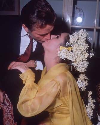 15th March 1964:  British-born Elizabeth Taylor sits on a sofa kissing her fifth husband, Welsh actor Richard Burton, while he leans over her on their first wedding day. Taylor is wearing a yellow gown and has flowers in her hair.  (Photo by Hulton Archive/Getty Images)