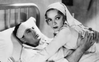 Actors Helen Hayes, as Catherine Barkley, and Gary Cooper, as Frederick Henry, embrace in a hospital bed in a scene from the 1932 version of A Farewell to Arms. | Based on: 'A Farewell to Arms' by Ernest Hemingway.