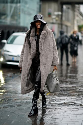 LONDON, ENGLAND - FEBRUARY 16: A guest wears a shiny pvc bob hat, a gray fluffy faux fur long coat, black shiny pvc high boots, a gray leather bag, during London Fashion Week Fall Winter 2020 on February 16, 2020 in London, England. (Photo by Edward Berthelot/Getty Images)