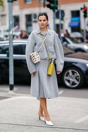 MILAN, ITALY - SEPTEMBER 20:  Doina Ciobanu wears a light grey wool oversized jacket, a light grey split skirt, a white woven leather openwork cylindric bag, a yellow leather bottle holder, white pointy mules, outside the Sportmax show during Milan Fashion Week Spring/Summer 2020 on September 20, 2019 in Milan, Italy. (Photo by Edward Berthelot/Getty Images)