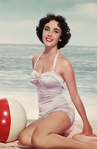 Elizabeth Taylor poses in a swimsuit with a beach ball.