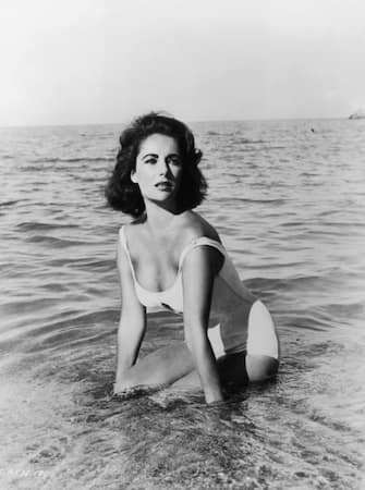 1959:  British born actor Elizabeth Taylor wears a white swimsuit while kneeling in the surf in a still from director Joseph L Mankiewicz's film 'Suddenly Last Summer'.  (Photo by Hulton Archive/Getty Images)