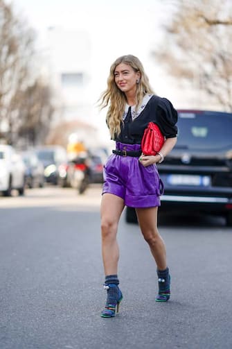 1208048700 MILAN, ITALY - FEBRUARY 22: Emili Sindlev wears a ruffled black shirt with puff shoulder pads, a red quilted bag, purple leather shorts, gray wool socks, multicolor shoes, outside MSGM, during Milan Fashion Week Fall/Winter 2020-2021 on February 22, 2020 in Milan, Italy. (Photo by Edward Berthelot/Getty Images)
