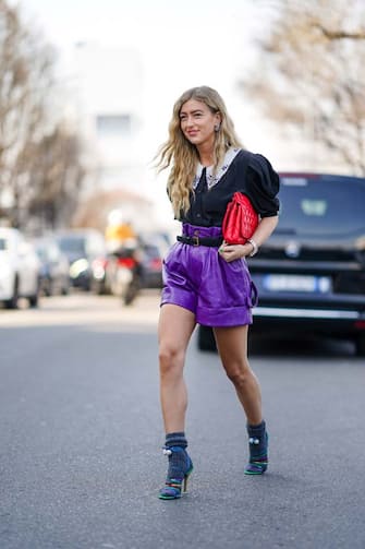 MILAN, ITALY - FEBRUARY 22: Emili Sindlev wears a ruffled black shirt with puff shoulder pads, a red quilted bag, purple leather shorts, gray wool socks, multicolor shoes, outside MSGM, during Milan Fashion Week Fall/Winter 2020-2021 on February 22, 2020 in Milan, Italy. (Photo by Edward Berthelot/Getty Images)