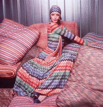 Portrait of a model wearing a colorful outfit designed by Missoni while posing on pillows covered in Missoni fabric. The outfit consists of a herringbone weave head scarf and maxi skirt and a striped top.   (Photo by Hulton Archive/Getty Images)