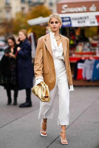 PARIS, FRANCE - SEPTEMBER 25: Caroline Daur wears earrings, necklaces, a camel leather oversized jacket, a white shirt, white wide-legs crop pants, white sandals, a shiny gold puff bag, outside Rochas, during Paris Fashion Week - Womenswear Spring Summer 2020 on September 25, 2019 in Paris, France. (Photo by Edward Berthelot/Getty Images)