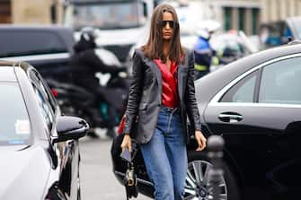 PARIS, FRANCE - FEBRUARY 28: A guest wears sunglasses, a black leather blazer jacket, a red shiny glittering double breasted top, blue denim jeans pants, a Dior Saddle bag, outside Balmain, during Paris Fashion Week - Womenswear Fall/Winter 2020/2021, on February 28, 2020 in Paris, France. (Photo by Edward Berthelot/Getty Images)
