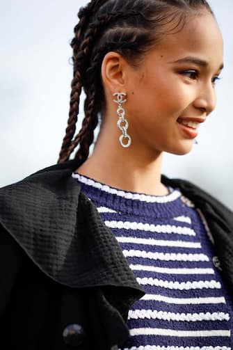 PARIS, FRANCE - MARCH 03: A guest wearing Chanel earrings, stripe shirt, white mini skirt, black coat and Chanel bag outside the Chanel show during Paris Fashion Week Womenswear Fall/Winter 2020/2021 Day Nine on March 03, 2020 in Paris, France. (Photo by Hanna Lassen/Getty Images)