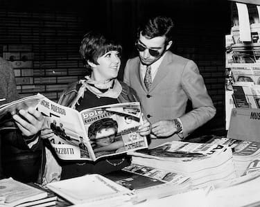 In front of a newspaper kiosk's counter, Italian singer Orietta Berti shows to her husband Osvaldo Paterlini an article about her, on the magazine Bolero. Italy, 1968.. (Photo by Mondadori via Getty Images)